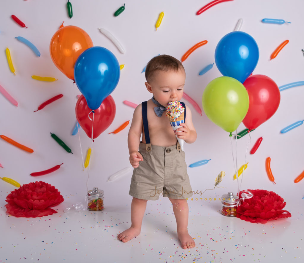 one year old boy eating ice cream cone with a sprinkles photography backdrop