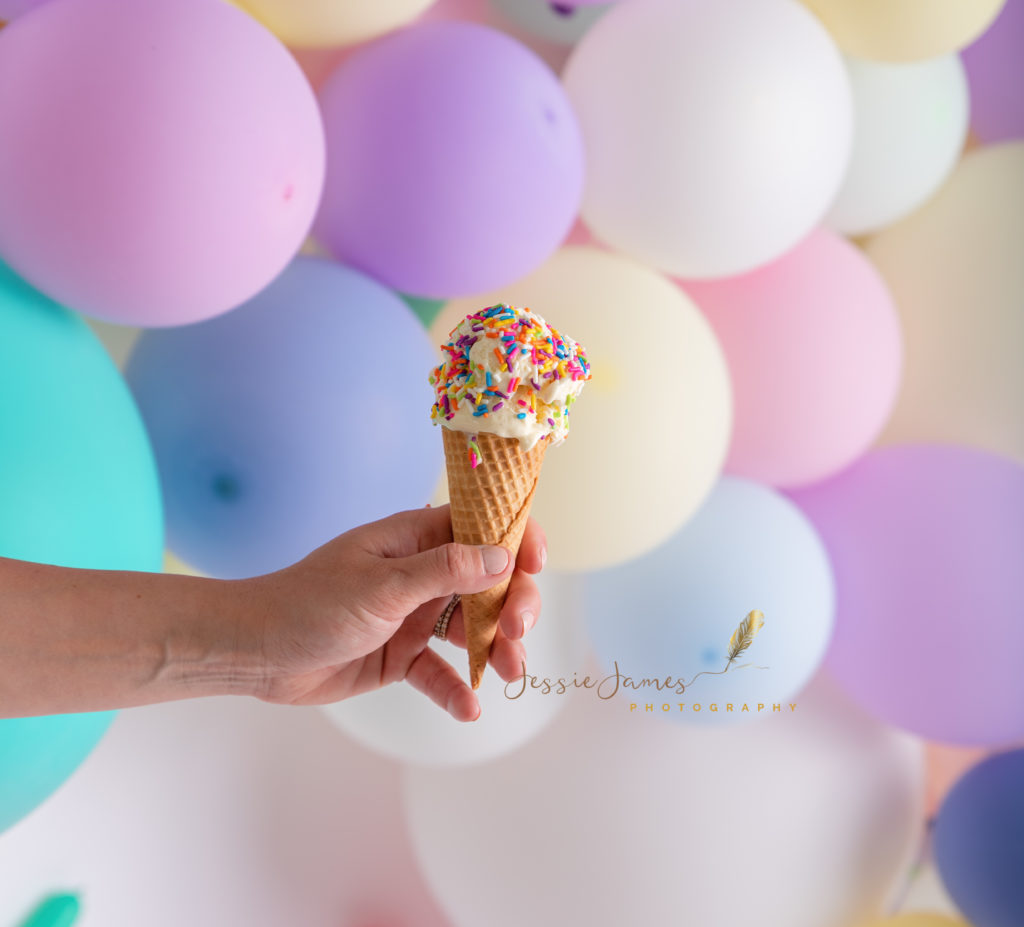 hand holding an ice cream cone in front of balloons