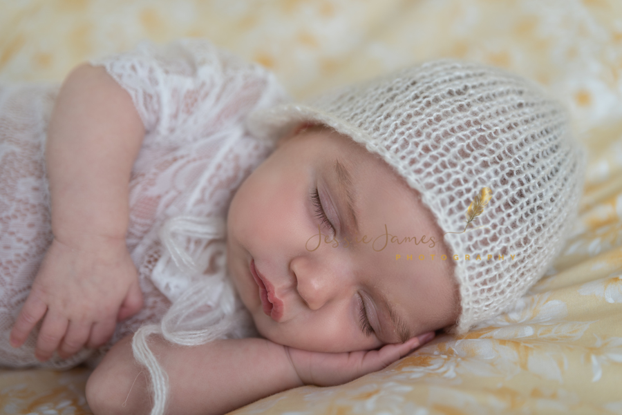 newborn baby girl sleeping on a yellow backdrop with a white  bonnet
