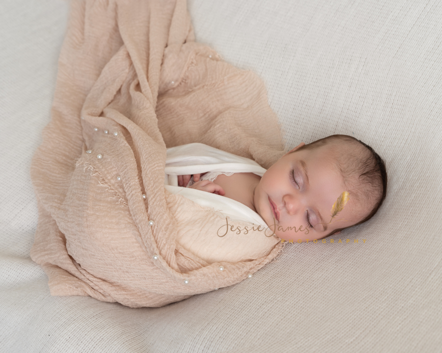 newborn baby girl wrapped in a nude blanket with pearls
