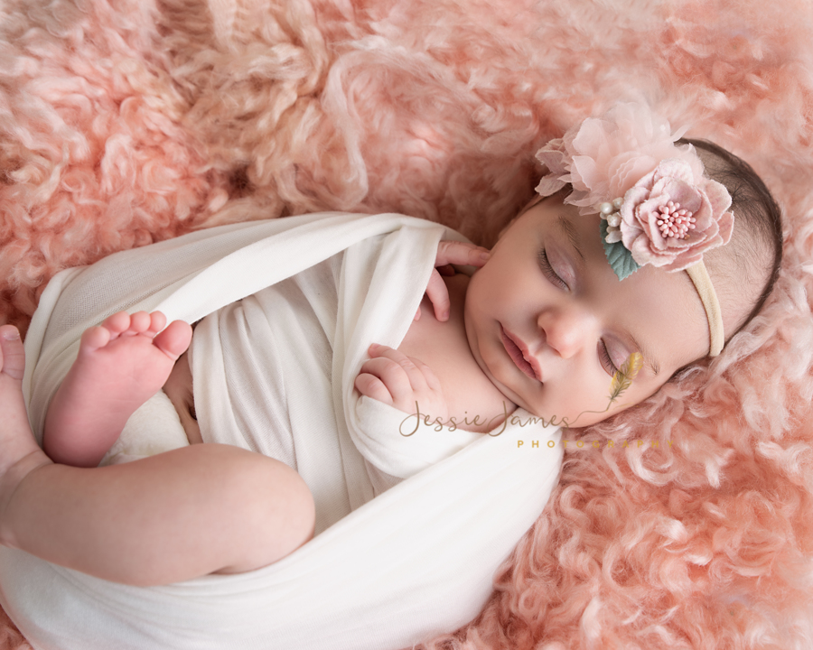 newborn baby girl wearing a floral headband sleeping on a pink flokati blanket, newborn photography poses, huck finn