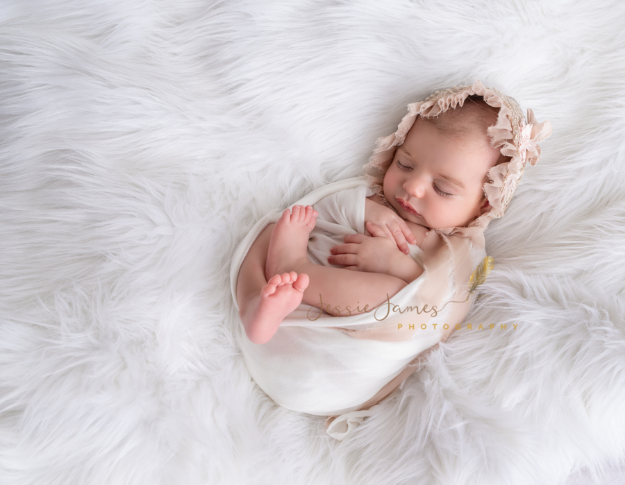 newborn baby girl sleeping on a plush white blanket with a pink bonnet