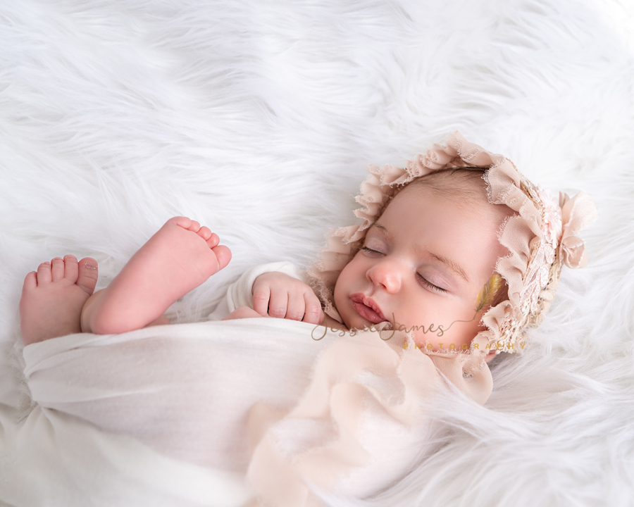 newborn baby girl sleeping on a white flokati wearing a white wrap