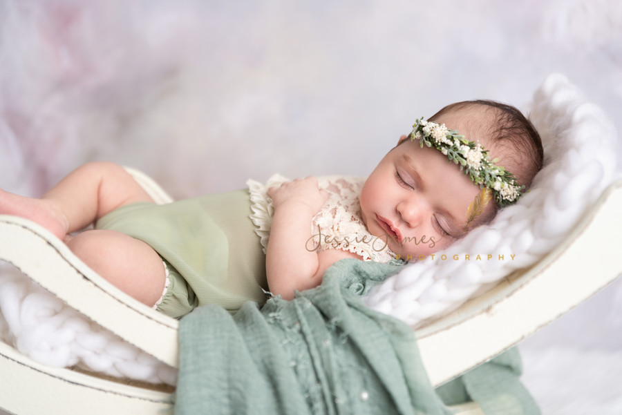 newborn baby girl wearing sage green outfit sleeping on anewborn bench prop