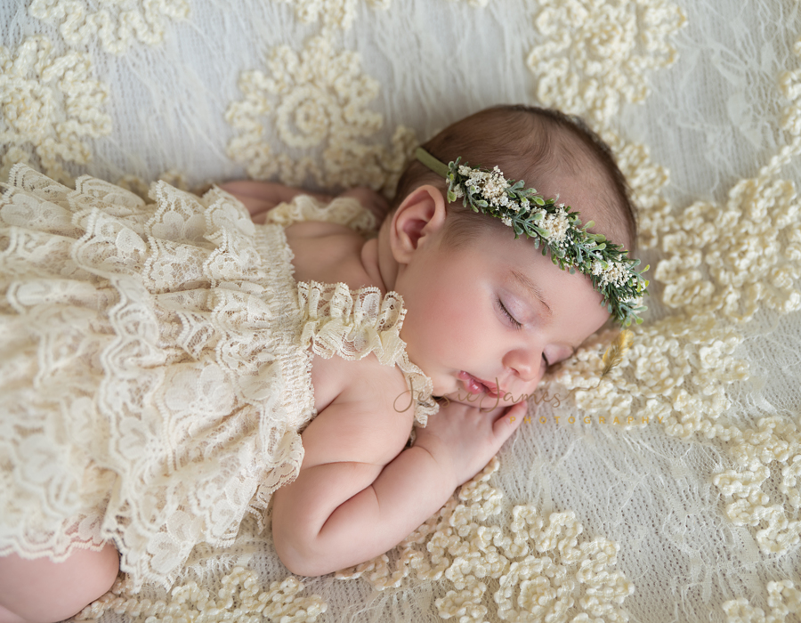 newborn baby girl in cream lace outfit and floral headband, baby girl laying on lace blanket
