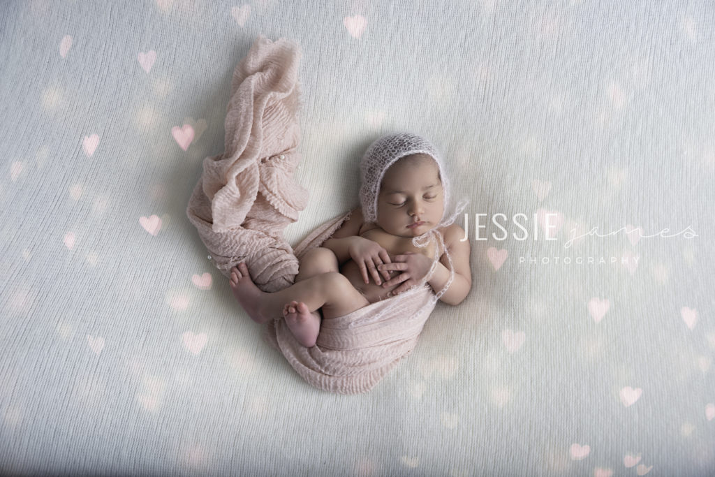 rainbow baby photoshoot, baby wrapped in pink pearl blanket on a white backdrop