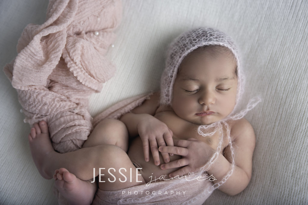rainbow baby portrait session, baby with pink bonnet wrapped in a pink blanket on a white backdrop