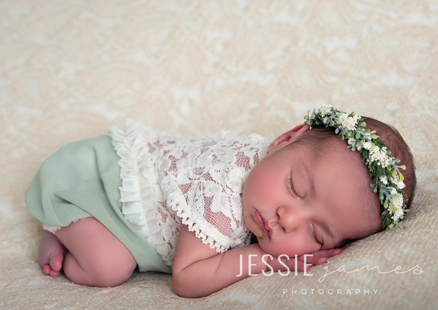 baby wearing sage green and a green floral headband on a beige lace blanket