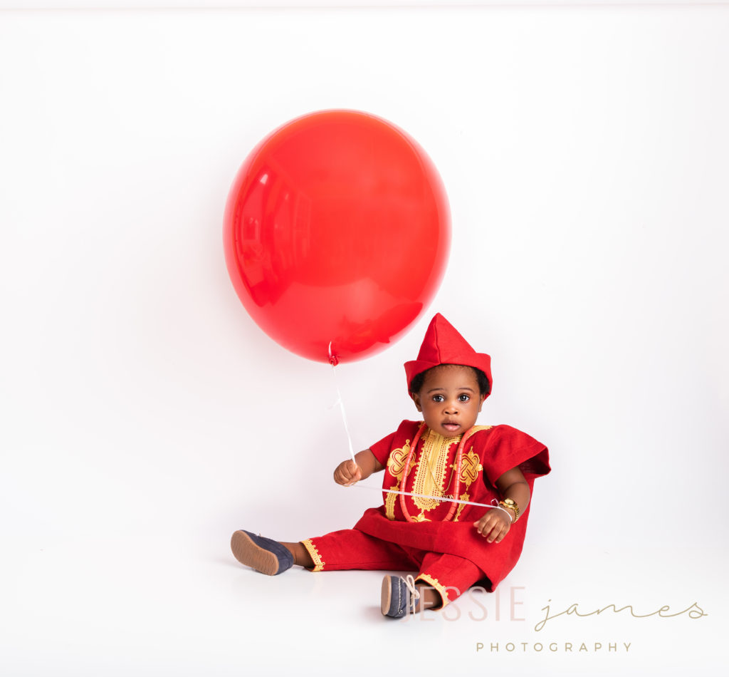 baby boy holding a red balloon wearing a red African outfit