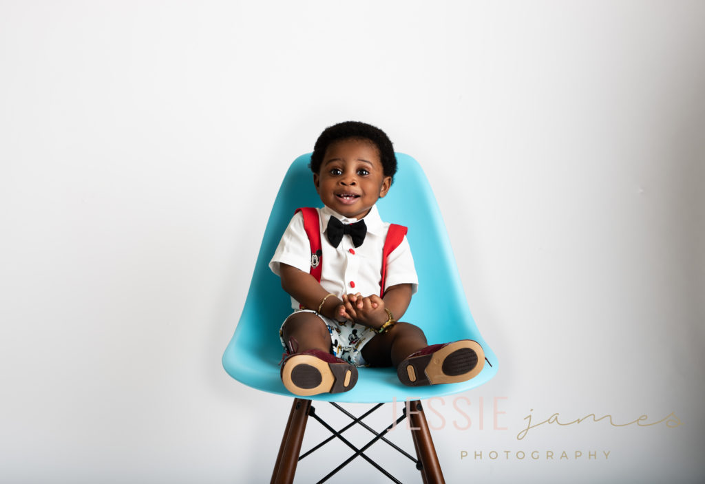 one year old boy sitting in a blue chair in front of a white backdrop