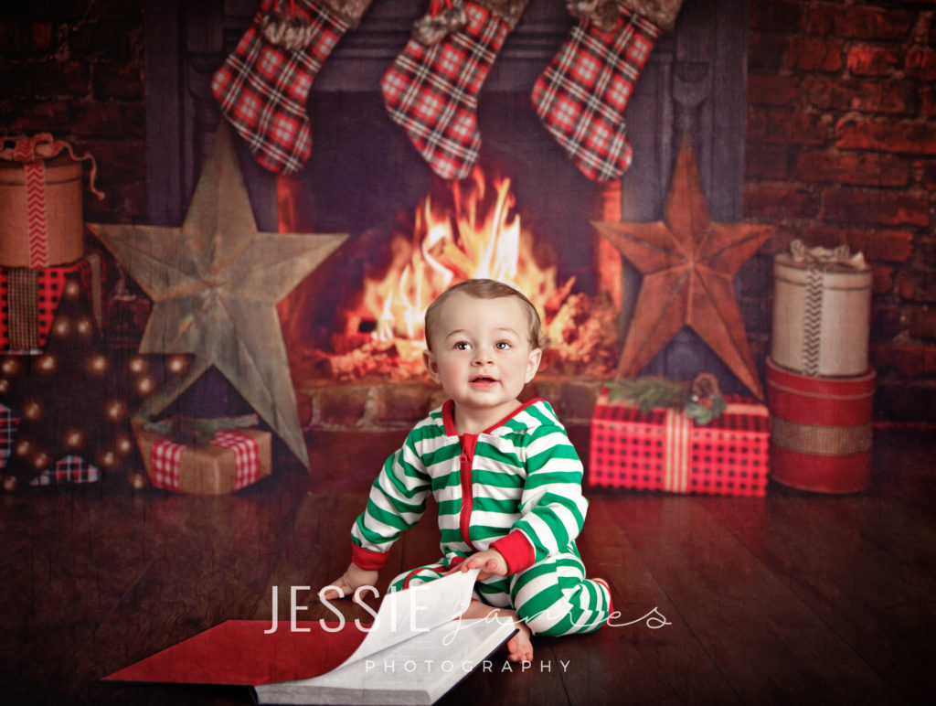 baby boy christmas portrait, baby wearing striped pajamas reading a christmas story by the fireplace