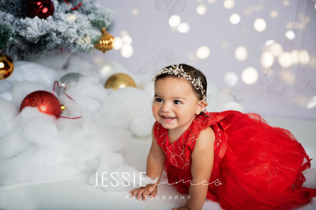holiday mini session photo, toddler girl sitting by a christmas tree