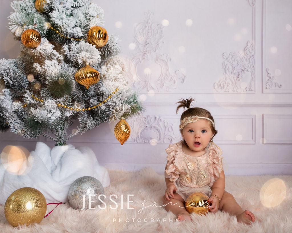baby christmas photo, baby girl holding an ornament sitting near a christmas tree