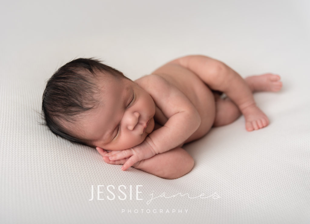 Newborn baby boy photography pose.  Baby sleeping in side laying position on a white backdrop.  Baby safely posed in a newborn photography pose.
