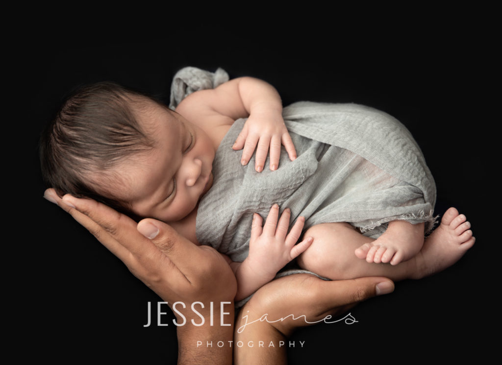 Newborn photography.  Baby boy sleeping in his fathers hands.  Low Key Photography uses dark tones to give a dramatic appearance.