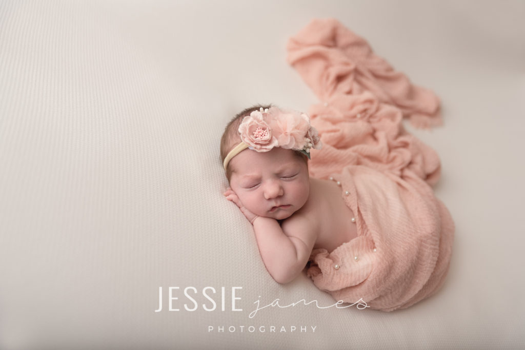 Newborn baby girl photography session.  Baby is sleeping on her belly with a pink wrap with pearls.