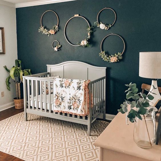 Dark accent wall in a nursery.  Nursery pictured has beautiful floral hoops on a dark green wall, and white crib to add some balance.  