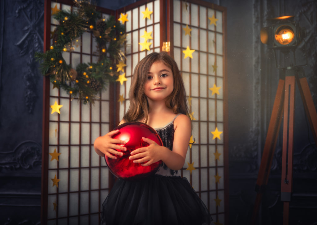 A little girl holding a red Christmas ornament.  