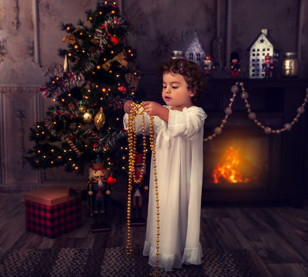 Christmas portrait of a little girl in a white vintage nightgown holding Christmas tree decorations. 