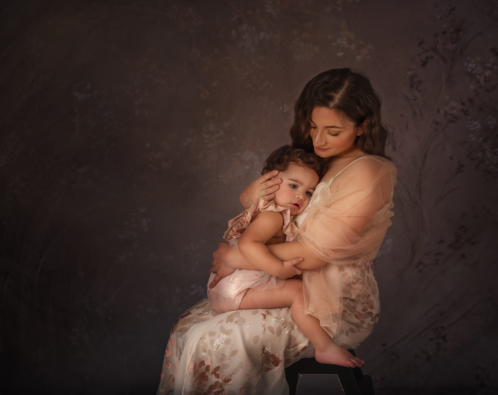 Mommy & Me Photography Session. Photo of a mother in a pink dress, cradling her young daughter. 