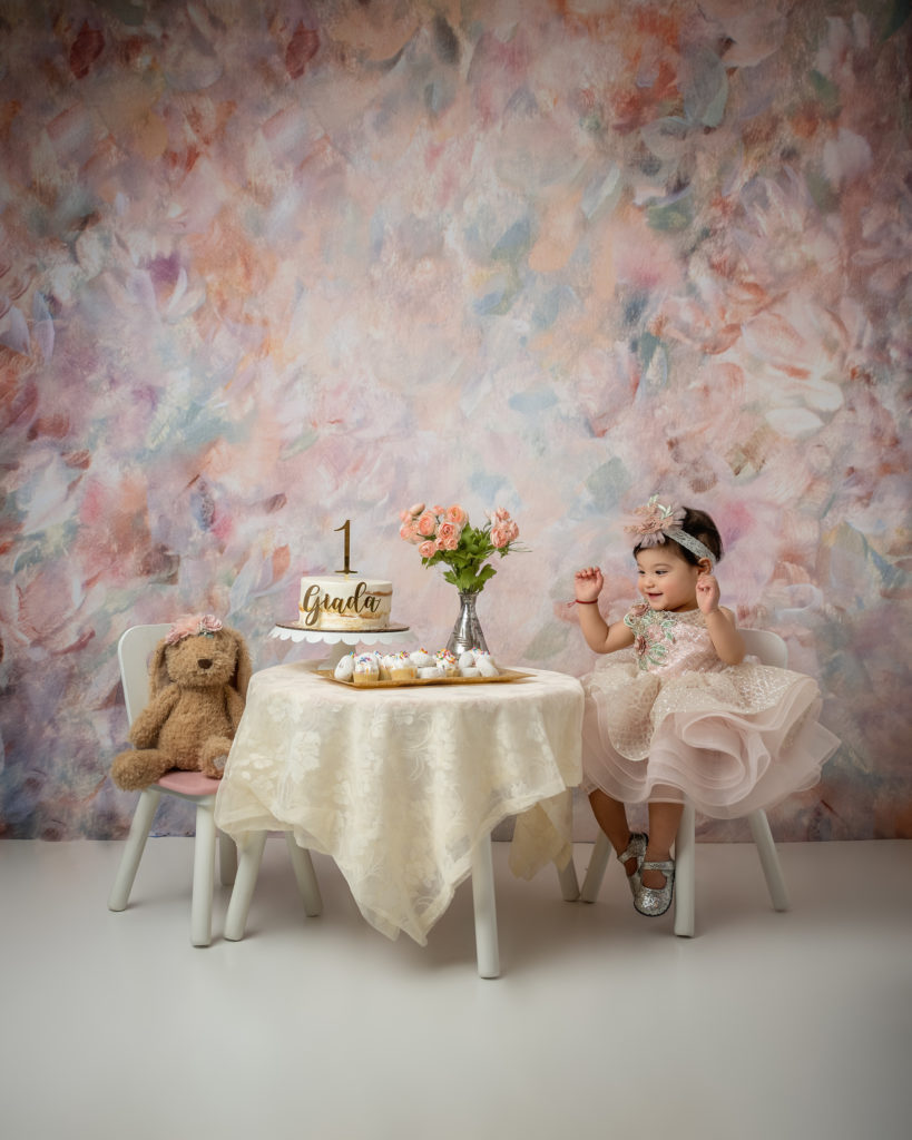 baby girl in pink dress having a tea party with a teddy bear. first birthday photo session
