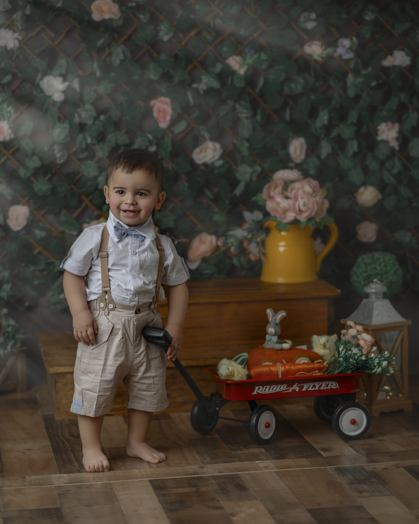Little boy in front of a green ivy wall with a radio flyer wagon filled with carrots. 