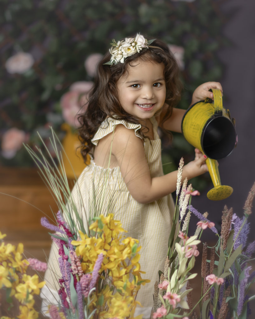 Little girl  in a yellow dress watering flowers. 