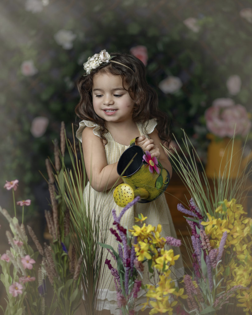 Sprin Mini Sessions, little girl in a yellow dress watering a garden of flowers. 