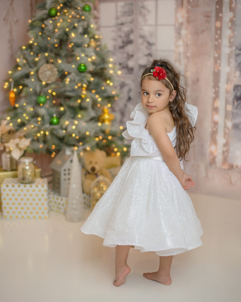 little girl in a white dress in front of a christmas tree