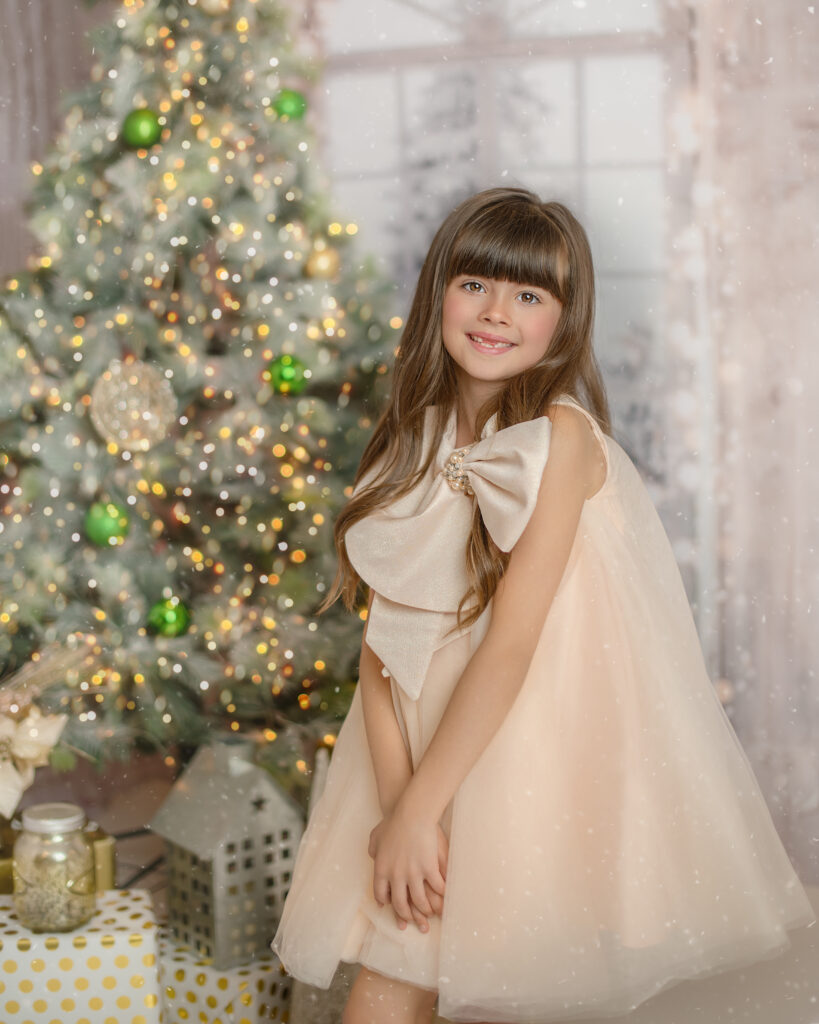 little girl in a peach dress in front of a christmas tree