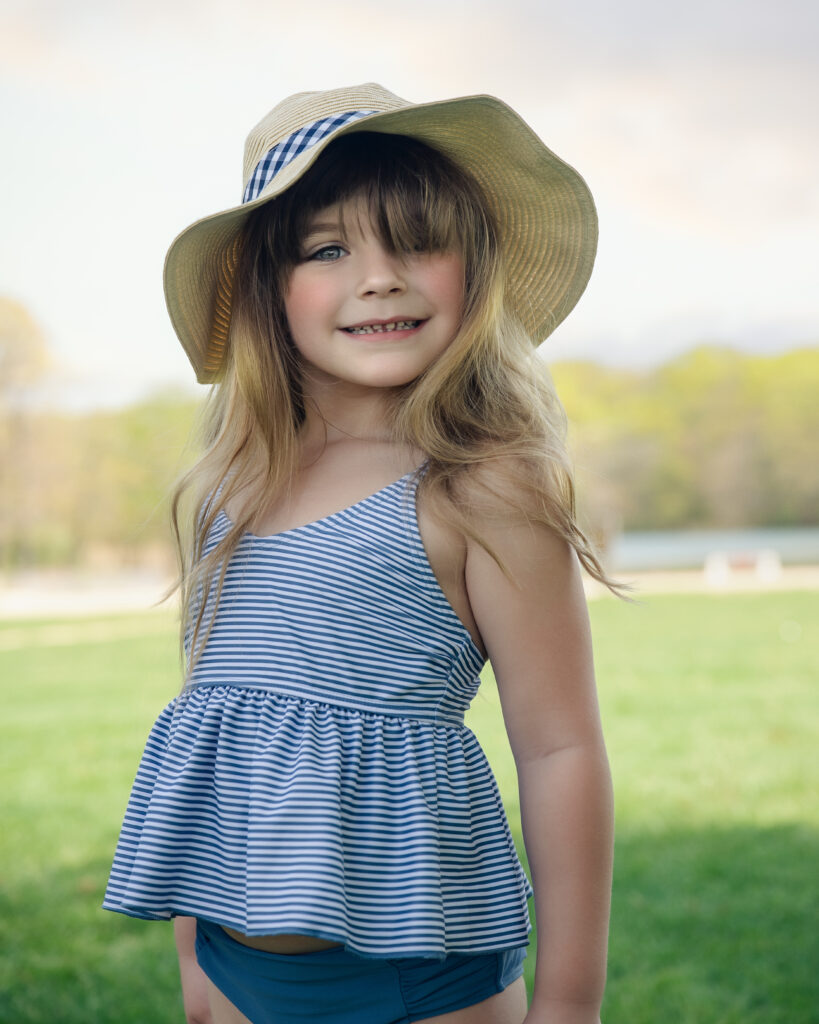 Little Girl in a cute hat posing in front of the lake for Summer Photography Session
