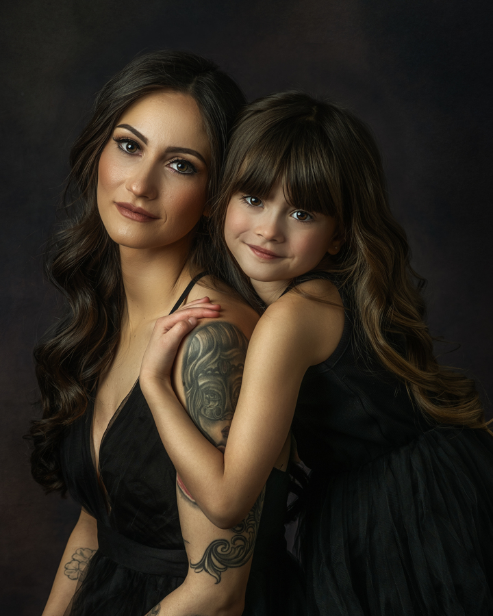 A mother and daughter, both in black gowns, embrace closely, gazing at the camera. The soft painterly lighting adds depth and a sense of intimacy, making the portrait feel like a classical painting.