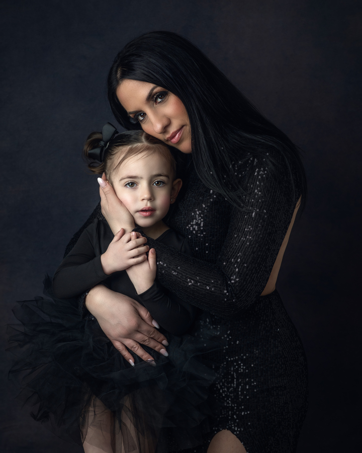 A mother in a shimmering black gown holds her young daughter in an editorial fine-art motherhood portrait. Captured during a luxury family photography session in New Jersey, this image highlights the deep connection between mother and child