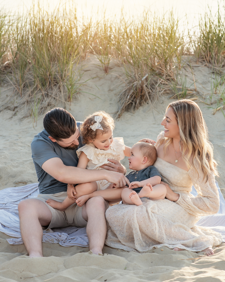 Family laughing and sitting together on the sand during New Jersey summer photo session at the beach in Middletown
