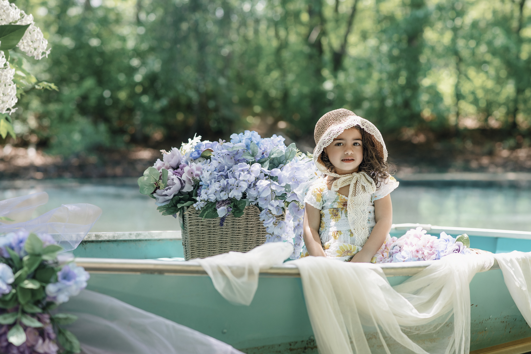 Little girl wearing sun hat sitting in a floral-decorated rowboat during New Jersey summer photo session in Freehold