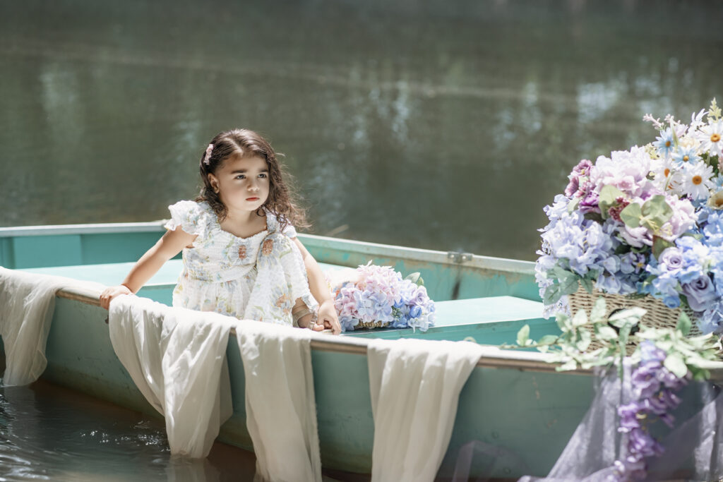 Young girl sitting in a vintage rowboat decorated with flowers during New Jersey summer photo session in Freehold