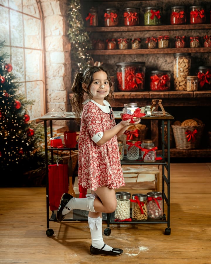 Little girl in a red vintage dress holds a jar with holiday cookies at the Christmas Cookie Cottage