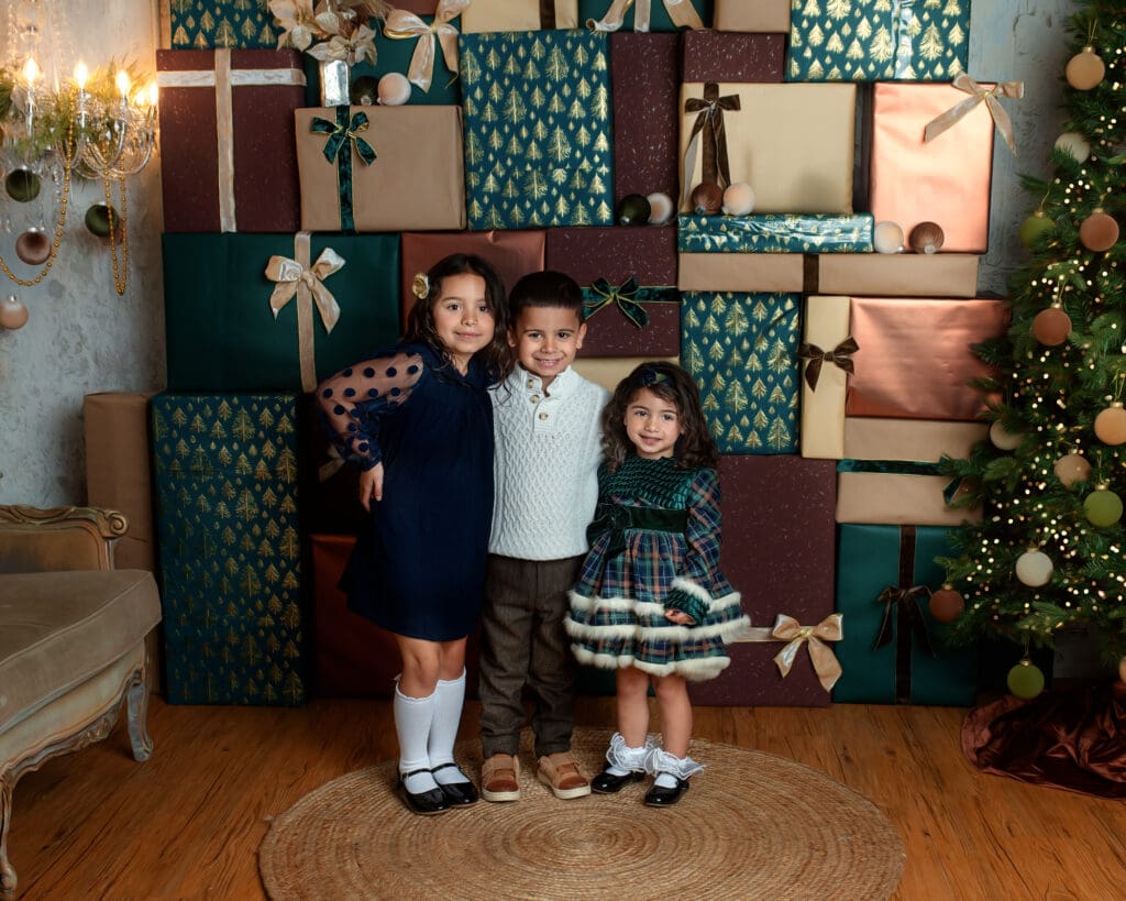 Three children dressed in classic holiday outfits stand in front of stacked presents in The Holiday Gift Stack set