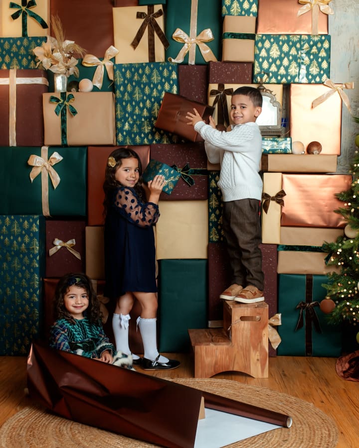 Three children play with wrapped gifts in The Holiday Gift Stack set during Christmas Mini Sessions